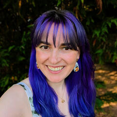 A picture of AM Ross. She is wearing a white and green sundress and has purple blue hair